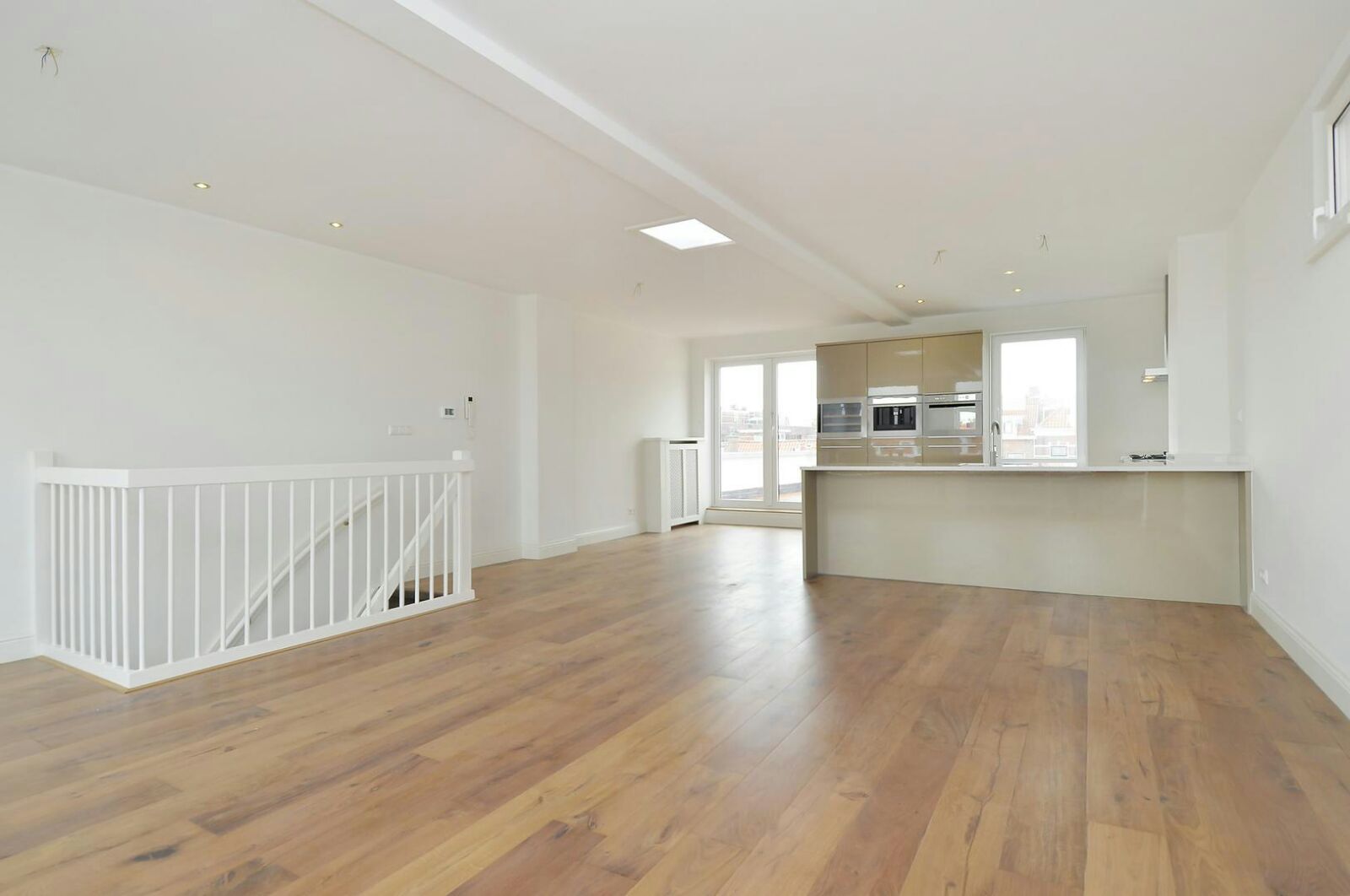 Lichte open ruimte met nieuwe houten vloer, witte trapbalustrade en de keuken achterin