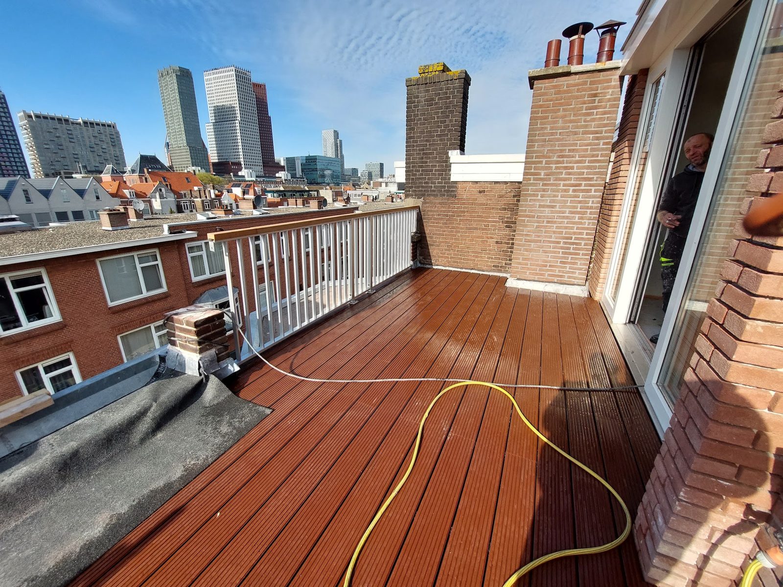 Dakterras met nieuwe hardhouten vlonder en wit hekwerk, met de skyline op de achtergrond